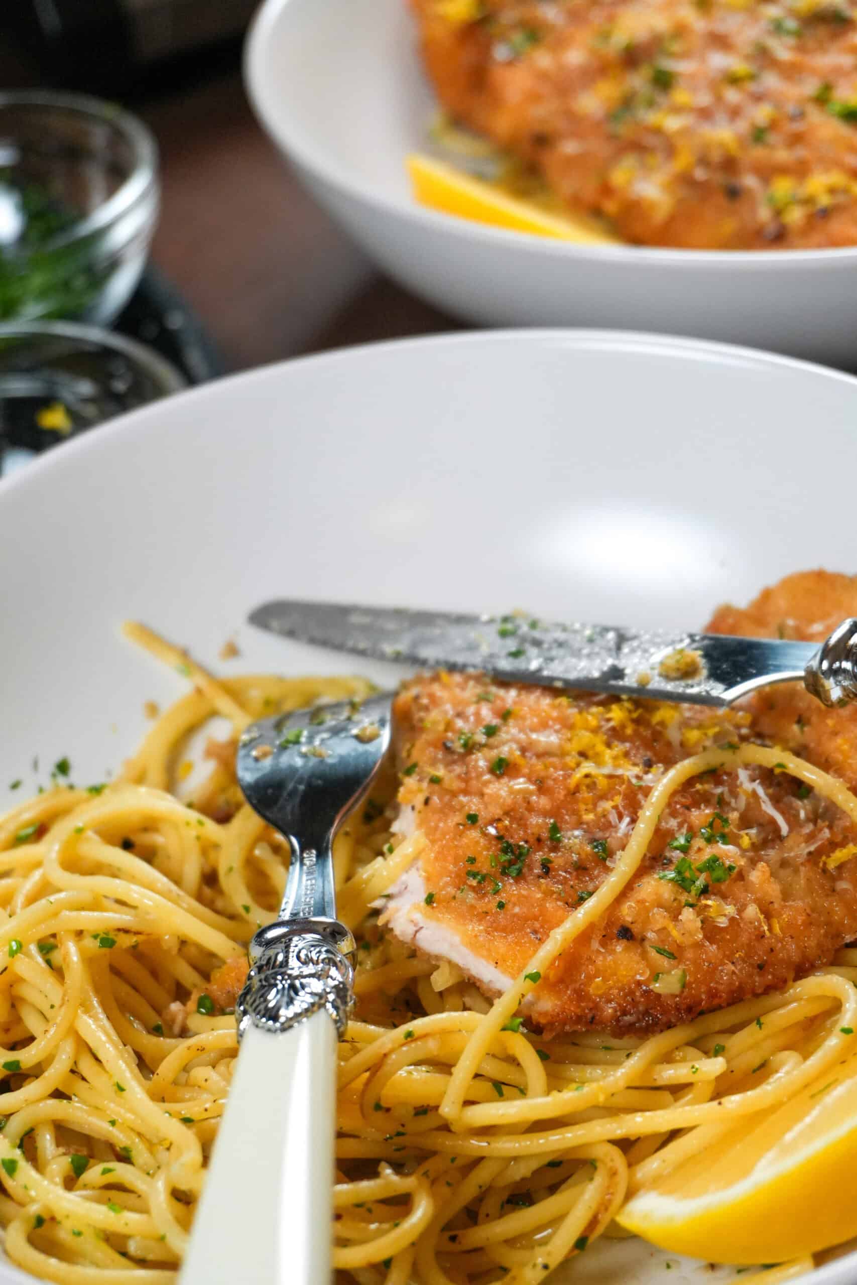 Crispy chicken cutlet with herb-infused spaghetti, garnished with lemon for a delightful dining experience.